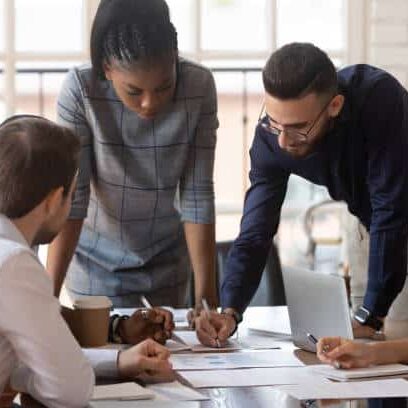 Focused multiracial corporate business team people brainstorm on marketing plan financial report gather at office table meeting, diverse serious colleagues group discuss paperwork engaged in teamwork